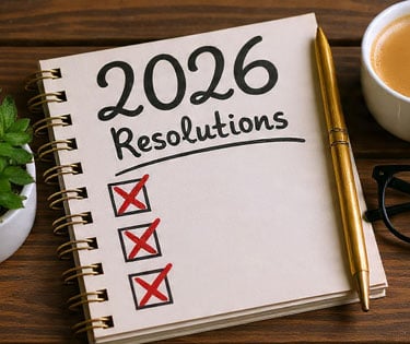 Notebook labeled “2026 Resolutions” with items crossed out, beside a coffee cup and glasses.