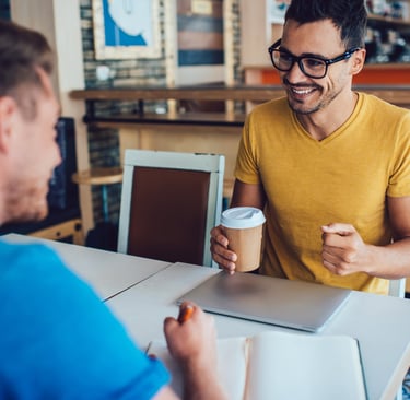 Two professionals having a coffee meeting, with one taking notes during an informational interview.