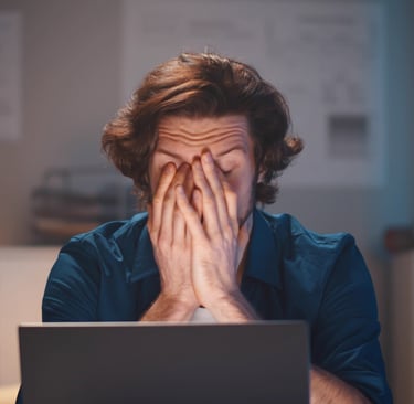 Person sitting at a laptop with hands covering face, showing frustration during a job search.