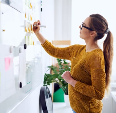 Woman writing on sticky notes on a whiteboard, representing planning and organization.