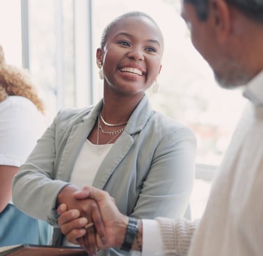 A smiling professional businesswoman shaking hands with a colleague during a networking event or meeting.