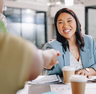 Professional smiling and shaking hands across a table during a meeting, suggesting a successful job 