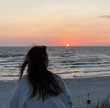 a woman standing on a beach with a sunset in the background