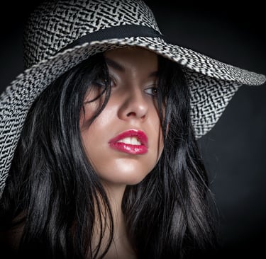 Porträt einer Frau mit schwarzem Haar und breitem Hut, aufgenommen im Studio mit dunklem Hintergrund – professionelles Beauty