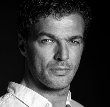 Schwarz-Weiß-Porträt eines Mannes mit dunklen Haaren, der direkt in die Kamera blickt.