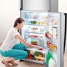 a woman is kneeling down to take a picture of a refrigerator