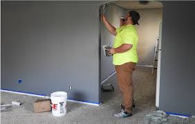 a woman in a yellow shirt is standing in a room with a paint roller