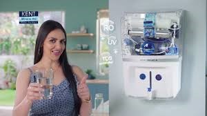 a woman holding a glass of water in front of a wall mounted water disp