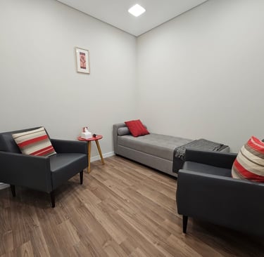 Ambiente de terapia com duas poltronas pretas com almofadas coloridas, uma mesa de madeira clara e j