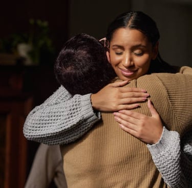 Uma mulher sorrindo abraça um homem em um ambiente acolhedor, transmitindo apoio e conforto