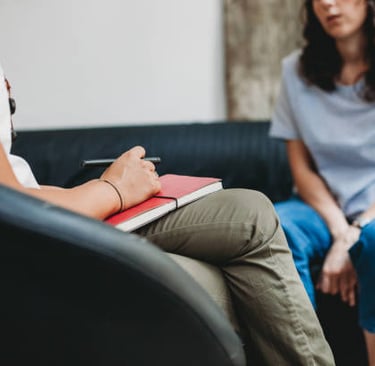 Um terapeuta com um caderno na mão, fazendo anotações durante uma sessão, enquanto o paciente a ouve