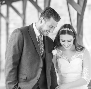 zoomed in black and white photo of bride and groom walking both laughing and smiling, archway framing them