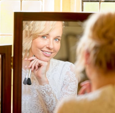 bride's reflection in the mirror looking into the camera lens with a big smile on her face