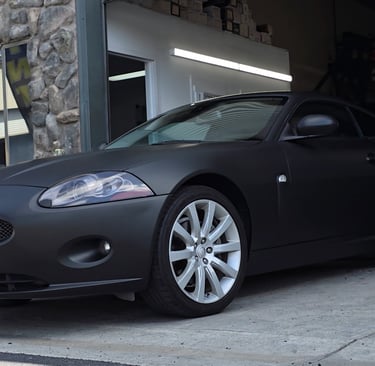 Matte black vinyl wrap on a Jaguar coupe , expertly installed in the shop.