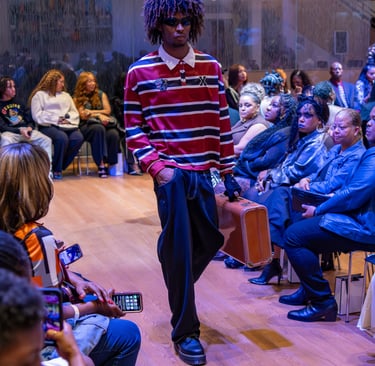 a man in a striped shirt and jeans walking down a runway