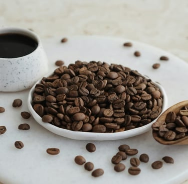 A plate filled with freshly roasted coffee beans with a mug of black coffee in the background