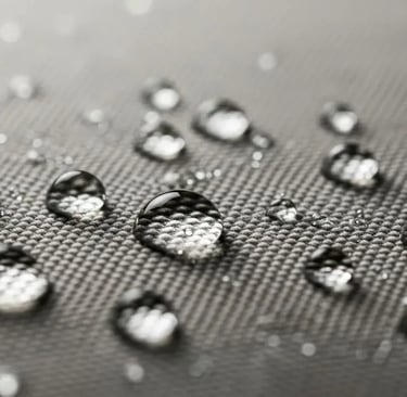 Tetesan air menggumpal di permukaan kain kanvas abu-abu, menunjukkan efek waterproof.