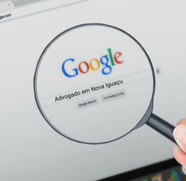 Lupa aproximando a barra de pesquisa do Google com a frase "Advogado em Nova Iguaçu" digitada, sobre