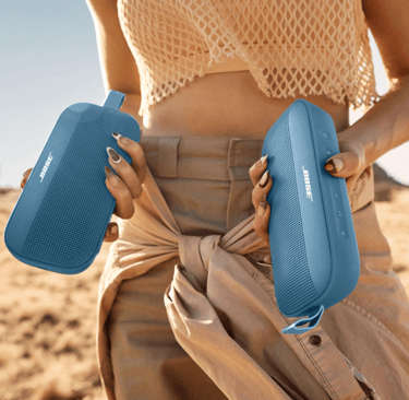 a woman in a tan dress holding a Bluetooth speakers