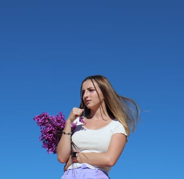 Photo of Audra Baruch underneath a sky holding purple flowers
