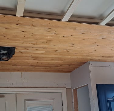 Partially installed wood plank ceiling with integrated ventilation fan in residential entryway levelled renovation project