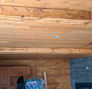 Wood-paneled ceiling with exposed beams and stone accent wall in rustic home interior renovation