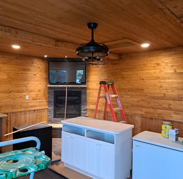 Rustic living room renovation in progress featuring wood-paneled ceiling and walls, stone fireplace, and new cabinetry