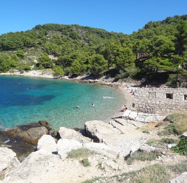 A secluded Croatian cove with clear turquoise water, a pebble beach, and lush green hills.