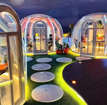 صف من الغرف الزجاجية المضاءة ليلاً في فضاء طبيعي واسع، مخصصة لجلسات طعام عائلية وخاصة