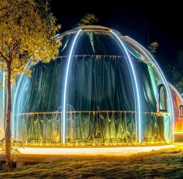 غرفة زجاجية على شكل فقاعة شفافة مضاءة ليلاً وسط الطبيعة، مهيأة لجلسة طعام خاصة