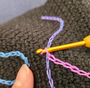 Close-up of a yellow crochet hook weaving colorful pink and purple yarn through black fabric.