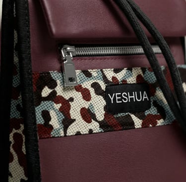 Close-up of a burgundy leather Yeshua crossbody bag featuring a patterned textile accent and silver zipper.