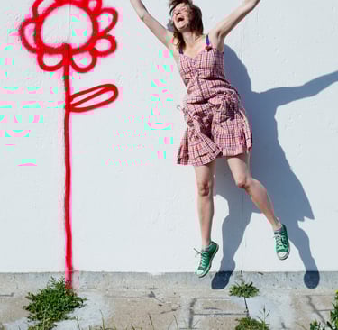 Phoebe Kreutz laughing and jumping next to a wall with a flower.