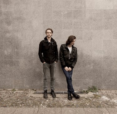 Two musicians standing against a wall.