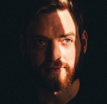 A headshot of a young man in the darkness light by a ray of light.