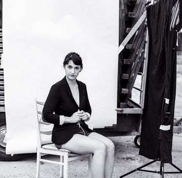 Actress Silvana Veit sitting outdoors in a black jacket and sneakers.