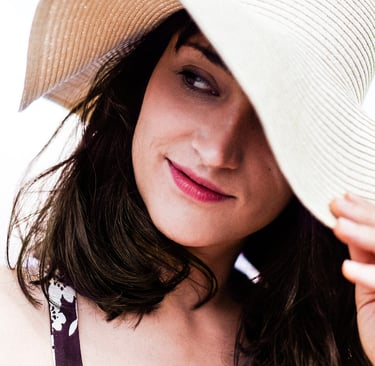 A headshot of an actress in a straw hat looking to the side.