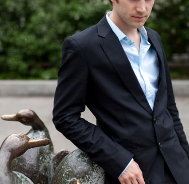 A man in a suit leaning on a fountain in a park.
