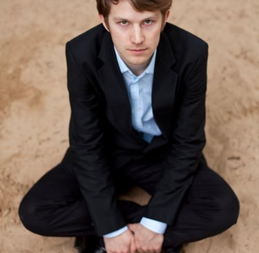 Tyson Naylor sitting on sand wearing a suit.