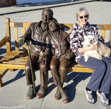 Anne on bench with dog and two bronze statues of elderly people.