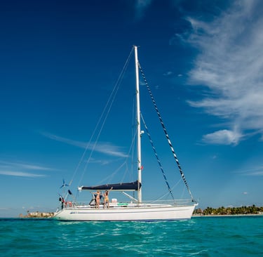 A white sailboat with two people on deck glides across turquoise ocean water under a clear blue sky, capturing the essence