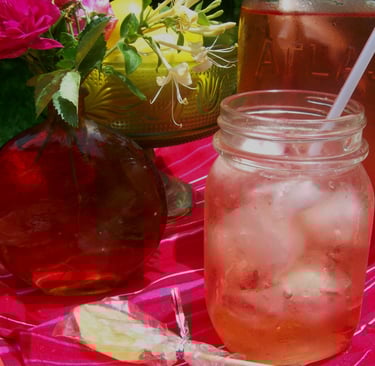 Mason jar with a fruity iced tea and a straw with green and red glass vases on a red tablecloth.