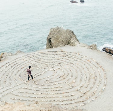 Eine Person ist in der Mitte eines runden Labyrinths an einer Klippe zum offenen Mehr hin.