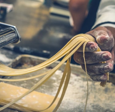 Close-up of a person’s hands making fresh tagliatelle with a pasta machine