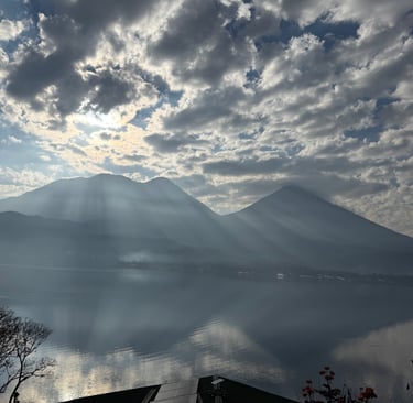 Sunlight rays piercing through clouds over a volcanic mountain lake landscape at dawn.