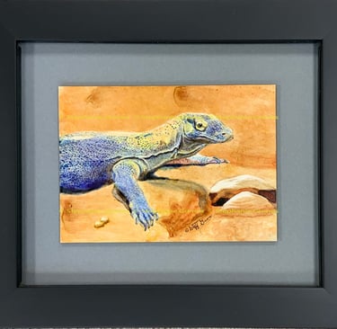 A framed ink painting of a blue and grey monitor lizard resting on orange sand.
