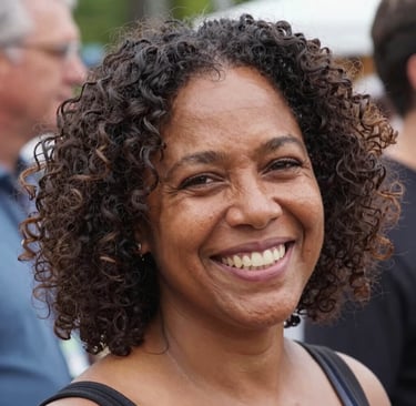 A smiling mature woman with dark curly hair and brown eyes in a close-up portrait.