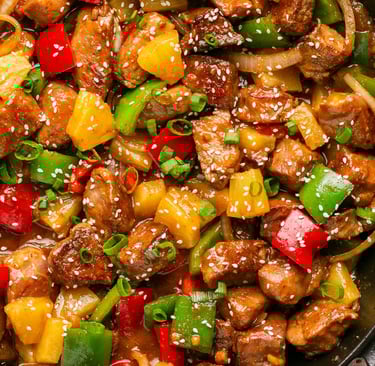 A plate of Sweet and Sour Pork with colorful bell peppers and pineapple chunks, served with steamed 