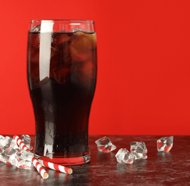 Glass of dark cola with ice cubes and striped paper straws on a red background — concept image relat