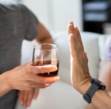A person holds up their hand in a clear "stop" gesture, refusing a glass of dark liquor being offered to them.